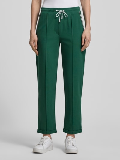 Frauenmodel trägt Straight Fit Stoffhose mit Ziernähten von Marc Cain aus Baumwoll-Modal-Mix, elastischer Bund mit Tunnelzug, fixierte Beinabschlüsse, 7/8-Länge, smaragdgrün, glatte Textur, Nahaufnahme Oberkörper. Kontext: Damen Stoffhose, Bundweite bei Größe 36: 39 cm, Innenbeinlänge 70 cm.