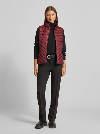 Vrouwenmodel draagt Slim Fit Steppweste mit Stehkragen van s.Oliver RED LABEL in effen bordeaux, met rits en opbergzak, ganzichaansicht van voren.