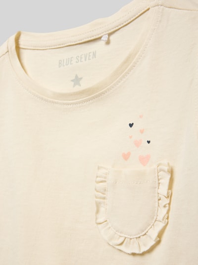 Mädchen trägt Regular Fit T-Shirt mit Rüschenbesatz von Blue Seven aus Reine Baumwolle, Brusttasche, Detailaufnahme Oberkörper.