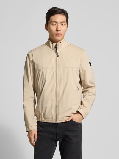 Männermodel trägt Jacke mit Stehkragen Modell 'Calvin' von Brax, beige, Baumwoll-Mix mit Reißverschlusstaschen, Ganzkörperansicht von vorne.