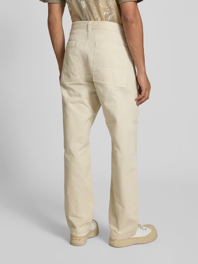 Männermodel trägt Straight Fit Hose aus Reiner Baumwolle von Forét in Beige mit Eingrifftaschen, Gesäßtaschen, Knopf- und Reißverschluss, Ganzkörperansicht Rückansicht.