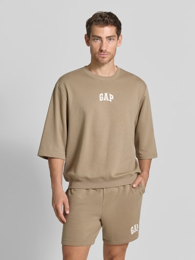 Männermodel trägt T-Shirt mit Rundhalsausschnitt und Logo-Print van GAP in beige, katoenmix, loose fit, ribboorden, logoprint, Ganzkörperansicht van voren