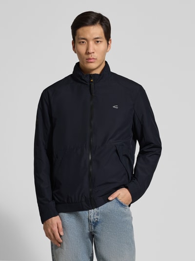Männermodel trägt Blouson mit Logo-Print und Stehkragen von camel active in Dunkelblau, Reißverschluss, gerader Schnitt, Ganzkörperansicht von vorne.