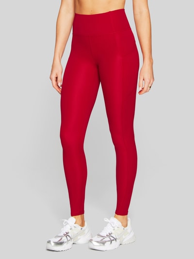 Frauenmodel trägt Slim Fit Leggins mit Beintaschen Modell 'OASIS' von Fabletics in Rot, elastischer Material-Mix, Ganzkörperansicht von vorne.