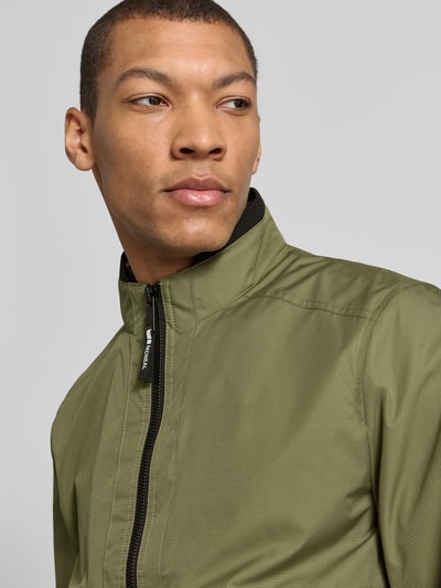 Männermodel trägt Regular Fit Jacke mit Stehkragen von MCNEAL in Olivgrün, mit Reißverschluss und Eingrifftaschen, Nahaufnahme Oberkörper. Rückenlänge bei Größe M: 64 cm, Schulterbreite: 43 cm, Brustweite: 55 cm, Ärmellänge: 67 cm.