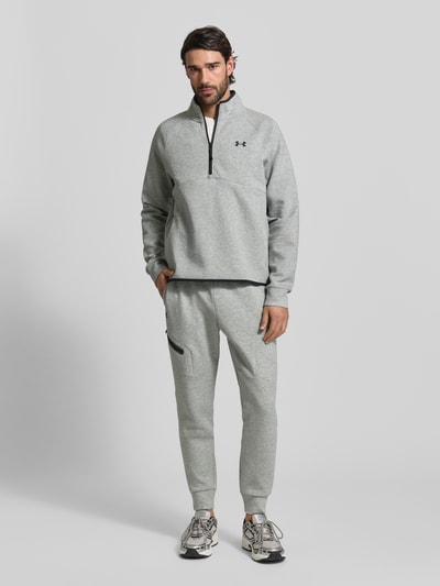 Männermodel trägt Regular Fit Sweatpants mit Logo-Print Modell 'Unstoppable' von Under Armour in Hellgrau mit elastischem Bund und Reißverschlusstasche, Material-Mix mit Baumwolle, Ganzkörperansicht von vorne.