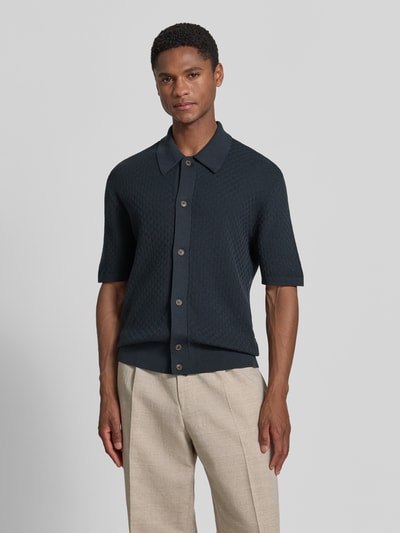Mężczyznę-model nosi koszulkę polo z fakturowanym wzorem Regular Fit model 'ARAAWEN' od Tiger Of Sweden z bawełny, krótki rękaw, kołnierzyk polo, listwa guzikowa, ciemny kolor, długość tyłu w rozmiarze M: 68 cm, długość rękawów w rozmiarze M: 28 cm, widok całej sylwetki z przodu.