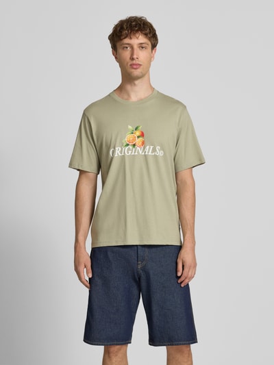 Mężczyzna model nosi Regular Fit T-Shirt mit Statement-Print Modell 'Eres' von Jack & Jones w kolorze jasnej oliwki, bawełna, okrągły dekolt, nadruk z przodu, kontekst: Herren T-Shirt von Jack & Jones, reine Baumwolle, krój regular fit, Modell 'Eres', statement print, okrągły dekolt, długość tyłu w rozmiarze M: 61 cm, Ganzkörperansicht von vorne