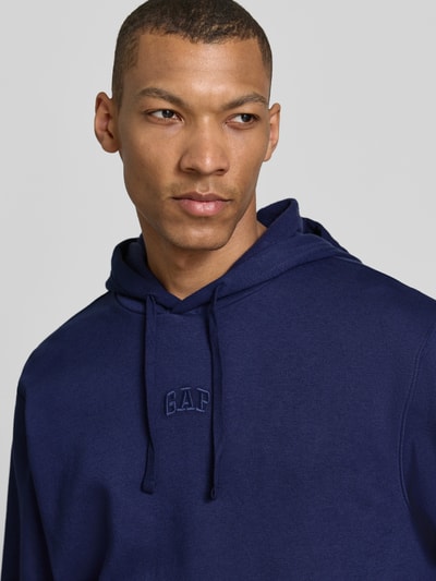 Männermodel trägt Oversized Hoodie mit Logo-Stitching von GAP in Dunkelblau, Baumwoll-Mix, Kapuze mit Tunnelzug, Nahaufnahme Oberkörper.
