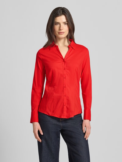 Frauenmodel trägt Regular Fit Hemdbluse in langärmeligen Design Modell 'Februar' von More & More, Hemdblusenkragen, tailliert, Baumwoll-Mix, durchgehende Knopfleiste, Rückenlänge 65 cm, Ärmellänge 60 cm, rote Farbe, glatte Textur, Ganzkörperansicht von vorne.