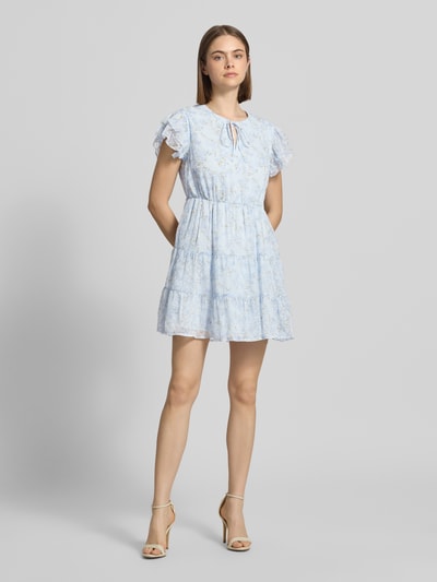 Frauenmodel trägt tailliertes Freizeitkleid mit Volants Modell 'ELIZA' von Only, florales Allover-Muster in Hellblau, Crinkle-Design, Mini-Länge, Rundhals-Ausschnitt, Ganzkörperansicht von vorne.