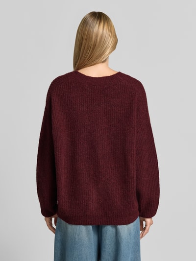 Frauenmodel trägt Oversized Cardigan mit Alpaka-Anteil Modell 'East' von American Vintage in Strick-Optik, dunkelrot, Ganzkörperansicht Rückansicht.