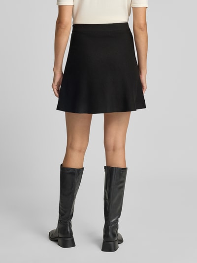 Frauenmodel trägt Ausgestellter Mini-Rock aus Viskose-Baumwoll-Mix Modell 'ELLY' von VERO MODA in Schwarz, Feinstrick, Volant-Saum, Ganzkörperansicht Rückansicht.