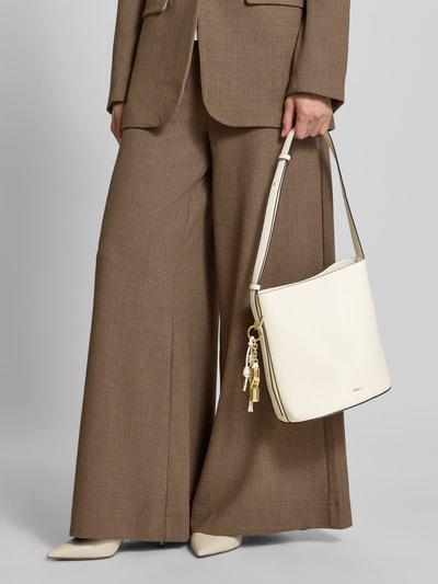 Frauenmodel trägt Handtasche aus Leder mit Label-Detail Modell 'ROXIE' von FURLA, cremefarben, mit Schulterriemen und Magnetverschluss, Nahaufnahme Oberkörper. Im Bild sichtbar: glatte Lederstruktur, rechteckige Form, Hauptfach, Reißverschluss-Innentasche, goldene Details. Breite 22 cm, Länge 25 cm, Tiefe 17 cm, Schulterriemen 112 cm.