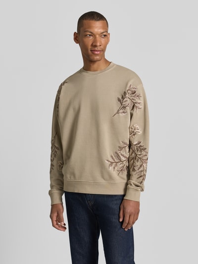 Männermodel trägt Regular Fit Sweatshirt Modell 'Kario' von Drykorn aus Reine Baumwolle mit florales Allover-Stitching, Rundhalsausschnitt, elastische Abschlüsse, Beige- und Brauntöne, Ganzkörperansicht von vorne.