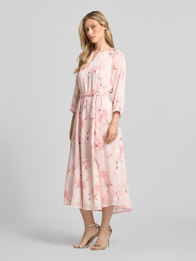Modelka kobieca nosi Midikleid mit Bindegürtel od More & More, jasnoróżowe, kwiatowy wzór, krój slim fit, pasek, rękaw 3/4, okrągły dekolt z wycięciem, tylny zamek błyskawiczny, szerokość w rozmiarze 36: 42 cm, długość tyłu: 128 cm, długość rękawa: 58 cm, widok całej sylwetki z przodu.
