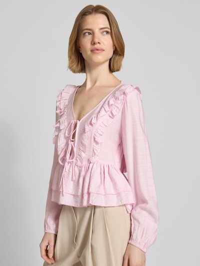 Modelka kobieca ma na sobie Regular Fit Langarmbluse aus Viskose-Mix Modell 'ZOEY' von Vero Moda w kolorze jasnoróżowym, z falbankami, marszczeniami i wiązaniem, długi rękaw z elastycznym mankietem, głęboki dekolt w serek, materiał z lyocellu, widok całej sylwetki z przodu.
