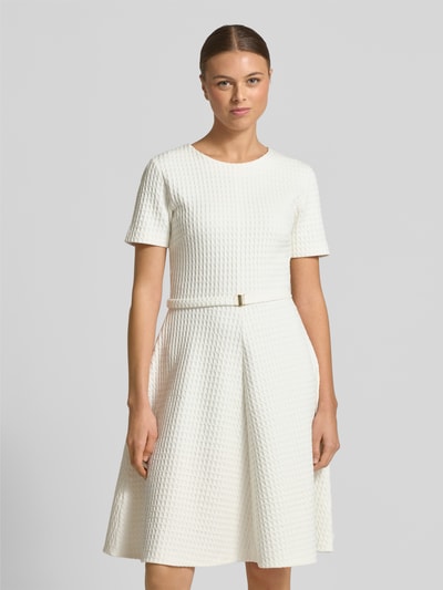 Kobiece modelka nosi Knielangens Kleid aus Baumwoll-Mix mit Strukturmuster od Marc Cain, mieszanka bawełny, linia A, taliowana, długość do kolan, krótkie rękawy, okrągły dekolt, detal z logo, odpinany pasek z materiału, długość pleców 97 cm, szerokość klatki piersiowej 43 cm, długość rękawa 22 cm, całość w jasnym kolorze, fakturowana powierzchnia, widok na cały przód sylwetki.