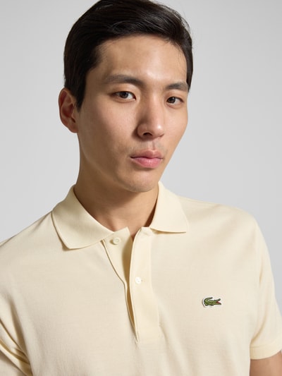 Männermodel trägt Regular Fit Poloshirt aus reiner Baumwolle von Lacoste in Beige mit Logo-Stitching, Nahaufnahme Oberkörper.