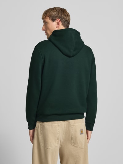 Männermodel trägt Hoodie mit Känguru-Tasche Modell 'BRADLEY' von JACK & JONES in Dunkelgrün, lockerer Schnitt, Ganzkörperansicht Rückansicht. Baumwoll-Materialmix, Kapuze mit Tunnelzug, sichtbare Struktur.