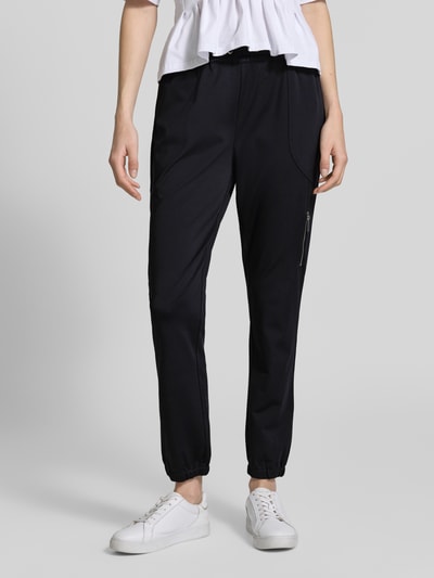 Frauenmodel trägt schwarze Damen Jogpants mit elastischem Bund, Tunnelzug und Stretch-Anteil von monari, Modell 'Jill', Regular-Fit, Material-Mix, Ganzkörperansicht von vorne. Bundweite 38 cm, Innenbeinlänge 75 cm bei Größe 36.
