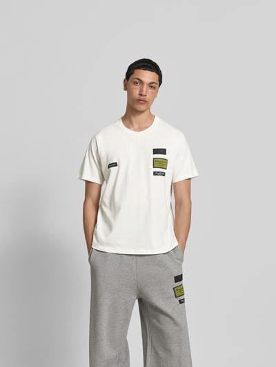 Männermodel trägt Relaxed Fit T-Shirt mit Logo-Patch von MM6 Maison Margiela aus reiner Baumwolle, Rundhalsausschnitt, kurzärmelig, Herren T-Shirt, Rückenlänge bei Größe M 80 cm, Ganzkörperansicht von vorne.