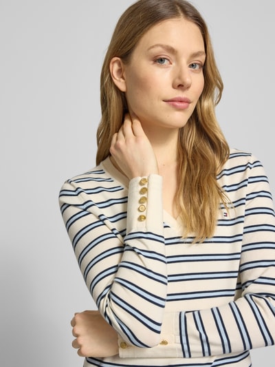 Vrouwenmodel draagt Regular Fit gebreide pullover uit puur katoen van Tommy Hilfiger met gestreepte look, logo-stitching, sierknopen, V-hals, lange mouw, geribd, detailopname bovenlichaam.