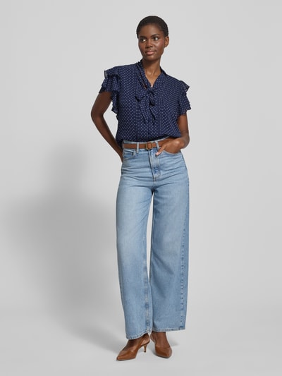 Frauenmodel trägt Regular Fit Schluppenbluse mit Volants Modell 'PRUGAN' von Lauren Ralph Lauren in Dunkelblau mit Tupfen, kurze Ärmel, Schluppe, Knopfleiste, kombiniert mit heller Jeans, Ganzkörperansicht von vorne.