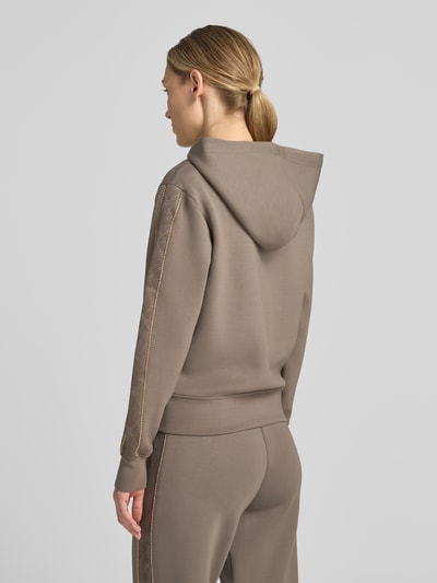 Frauenmodel trägt Relaxed Fit Sweatjacke mit Viskose-Anteil von GUESS in Taupe mit Zierbesatz und Kapuze, Ganzkörperansicht Rückansicht.