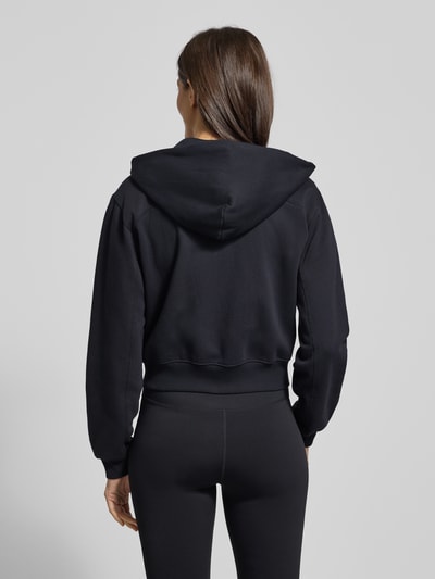 Frauenmodel trägt Sweatjacke mit Label-Stitching von Under Armour aus Baumwoll-Mix, Regular-Fit, Kapuze, Reißverschluss, Eingrifftaschen, Ganzkörperansicht Rückansicht.
