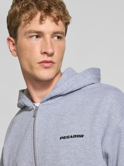 Männermodel trägt Regular Fit Sweatjacke aus Baumwoll-Mix von PEGADOR in Hellgrau mit Logo-Stickerei, Nahaufnahme Oberkörper.