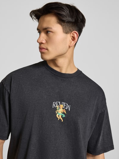 Männermodel trägt T-Shirt mit überschnittenen Schultern von REVIEW in Schwarz, lockerer Schnitt, Label-Print, reine Baumwolle, Nahaufnahme Oberkörper.