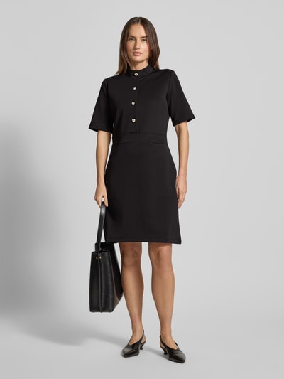 Frauenmodel trägt Kleid mit Stehkragen und Knopfleiste Modell 'Tibra' von JOOP!, schwarze Farbe, Material-Mix mit Baumwoll-Anteil, A-Linie, Mini, 1/2-Arm, glatte Textur, Ganzkörperansicht von vorne.