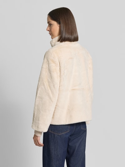 Modelka nosi kurtkę z sztucznego futra z wpuszczanymi kieszeniami Jacke aus Kunstfell mit Eingrifftaschen od COMMA, kremowy kolor, krój regular fit, stójka, zapięcie na guzik, długość tyłu w rozmiarze 36: 54 cm, szerokość ramion w rozmiarze 36: 40 cm, szerokość w biuście w rozmiarze 36: 56 cm, długość rękawa w rozmiarze 36: 66 cm, widok całej sylwetki z tyłu.
