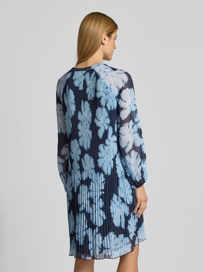 Frauenmodel trägt Knielanges Cocktailkleid mit Plisseefalten und Tunika-Ausschnitt von Christian Berg Cocktail aus Chiffon, Taillierter Schnitt, Ballonärmel, blickdichtes Unterkleid, Länge 99 cm, Brustweite 46 cm, Ärmellänge 58 cm, florales Muster in Blau, Ganzkörperansicht Rückansicht.