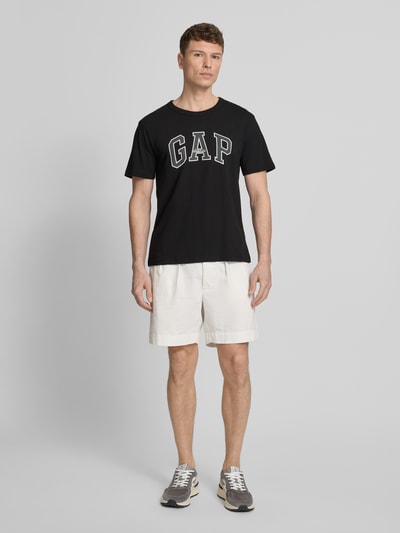 Männermodel trägt T-Shirt mit Logo und Rundhalsausschnitt von GAP aus Reine Baumwolle, Regular-Fit, schwarze Farbe, Ganzkörperansicht von vorne.