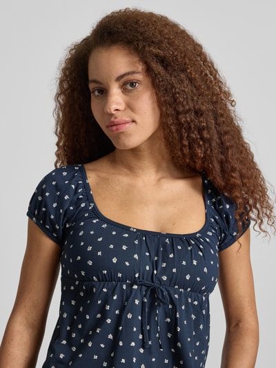 Frauenmodel trägt T-Shirt im Allover-Look mit Schnürung von REVIEW in Dunkelblau mit weißen Mustern, Nahaufnahme Oberkörper. Baumwoll-Elasthan-Mix, Regular Fit, Rundhalsausschnitt, Rückenlänge bei Größe S: 33 cm.