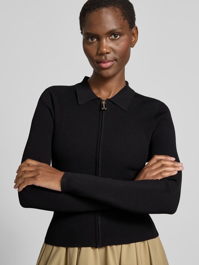 Frauenmodel trägt Slim Fit Jacke aus Viskose-Mix von Victoria Beckham in Schwarz mit Polokragen, Strick-Optik und Reißverschluss, Nahaufnahme Oberkörper. Rückenlänge bei Größe S: 49 cm.