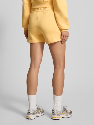 Kobiece modelka nosi Shorts mit Logo und elastischem Bund od adidas Sportswear w kolorze żółtym, materiał bawełniany, widok całej sylwetki z tyłu.