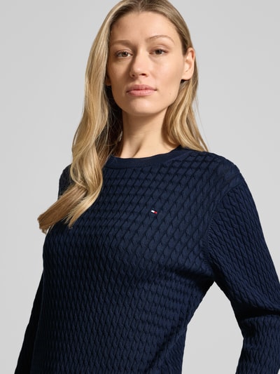 Frauenmodel trägt Slim Fit Pullover aus reiner Baumwolle von Tommy Hilfiger, Optik: Unifarben, Strickoptik, Zopfmuster, Logo-Detail, Rundhals, Langarm, Materialverarbeitung: Strick, Nahaufnahme Oberkörper.