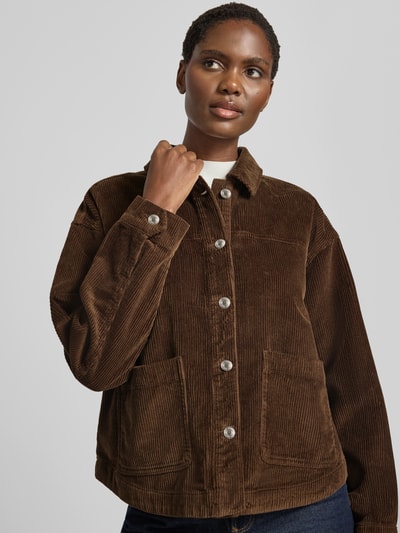 Frauenmodel trägt Relaxed Fit Langarmbluse aus reiner Baumwolle Modell 'JAMIE' von VERO MODA in Braun mit Knopfleiste und Taschen, Nahaufnahme Oberkörper.