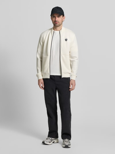 Männermodel trägt Sweatjacke mit Reißverschluss von EA7 Emporio Armani in Weiß, Regular Fit, Stehkragen, Ganzkörperansicht von vorne.