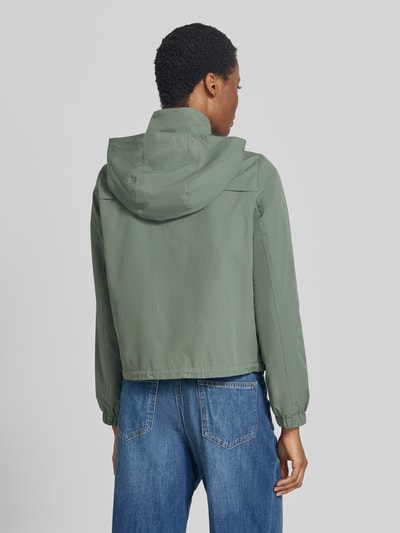 Frauenmodel trägt Regular Fit Parka mit Kapuzenkragen Modell 'ZOA' von VERO MODA in mattem Grün, kombiniert mit blauen Jeans, Ganzkörperansicht Rückansicht.