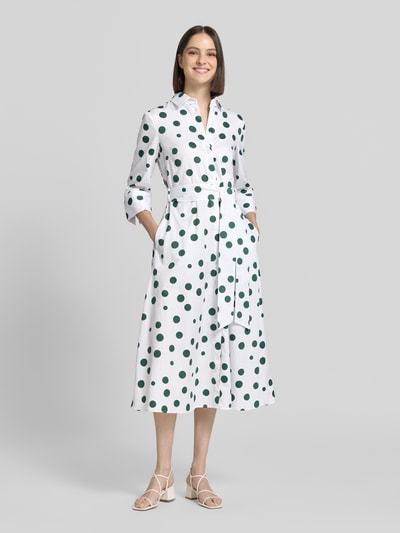 Frauenmodel trägt Hemdblusenkleid aus reiner Baumwolle von Christian Berg Woman, weiß mit grünen Punkten, Taillierter Passform, Hemdblusenkragen, 3/4-Arm, durchgängige Knopfleiste, Taillienband, Ganzkörperansicht von vorne. Rückenlänge 121 cm, Brustweite 46 cm, Ärmellänge 48 cm, Größe 36.