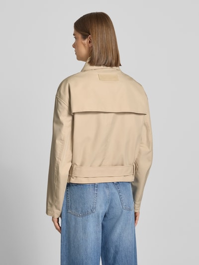Modelka kobieca ma na sobie Relaxed Fit Trenchcoat aus Baumwoll-Mix od Tommy Jeans, beżowy bawełniany twill, długość cropped, z paskiem, widok całej sylwetki z tyłu.