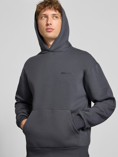 Männermodel trägt Relaxed Fit Sweatshirt aus katoenmix met kangoeroezak van REVIEW in donkergrijs, labeldetail, Nahaufnahme Oberkörper. Ruglengte maat M 68 cm, mouwlengte maat M 62 cm.