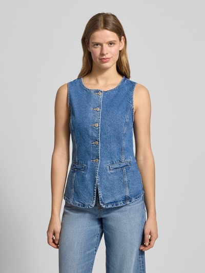 Frauenmodel trägt Jeansweste aus reiner Baumwolle Modell 'GUILINA' von ONLY in blauer Denim-Optik, Paspeltaschen, Rundhals, einreihige Knopfleiste, Ganzkörperansicht von vorne.