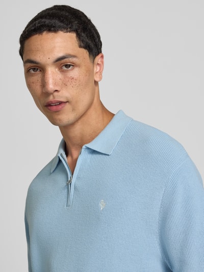 Męski model nosi Boxy Fit Poloshirt mit Logo-Stitching od REVIEW, koszulka polo z bawełny, kołnierzyk polo, zamek błyskawiczny; zbliżenie na górną część ciała.