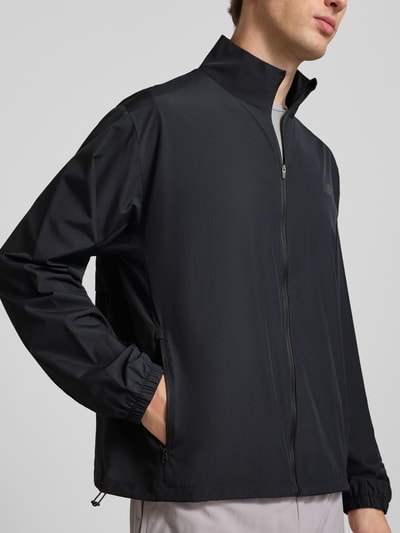 Männermodel trägt schwarze Regular Fit Jacke in Stehkragen Modell 'Fast Days' von New Balance mit Logo-Print, Nahaufnahme Oberkörper.
