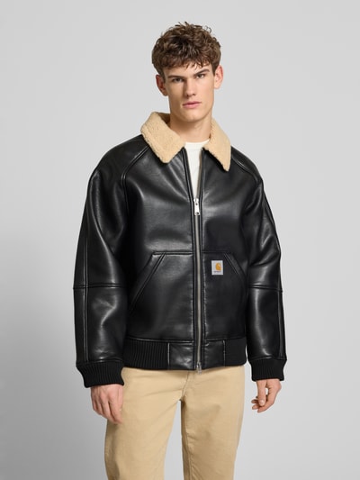 Männermodel trägt schwarze Bomberjacke mit Zweiwege-Reißverschluss Modell 'SHEPTON' von Carhartt Work In Progress, Umlegekragen mit Teddyfell, Eingrifftaschen, Label-Detail, Relaxed Fit, Ganzkörperansicht von vorne.